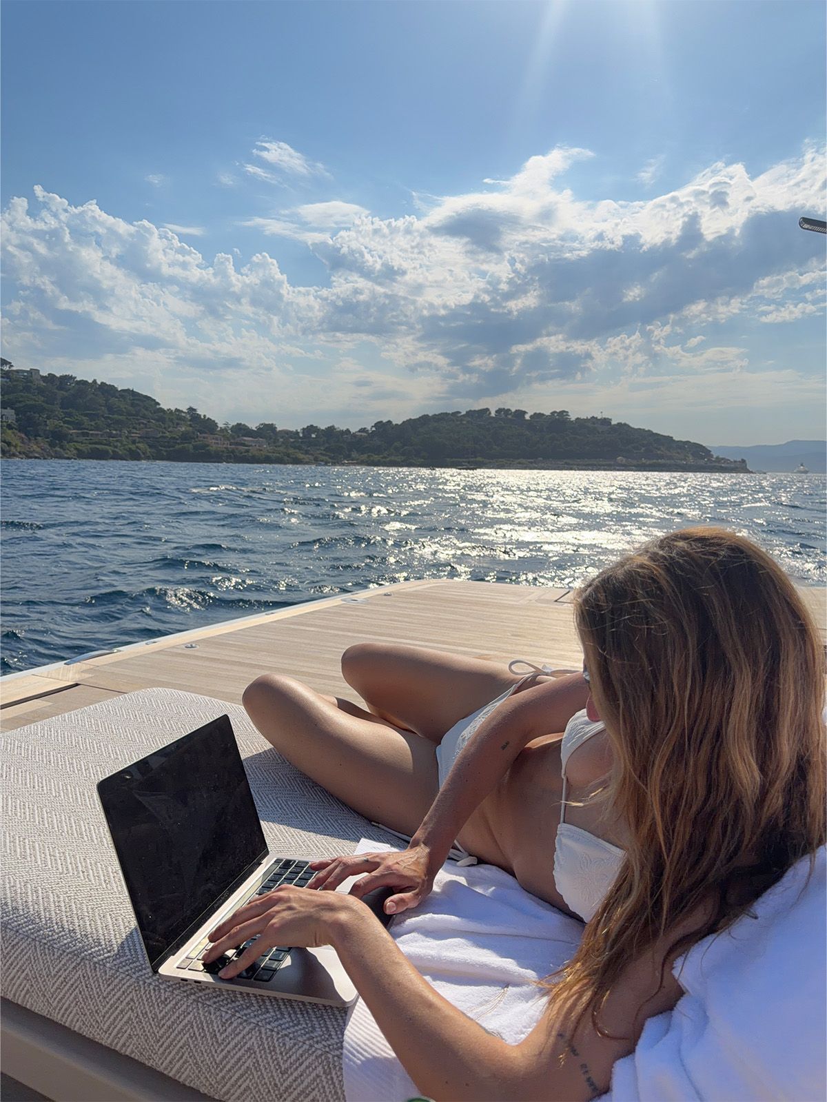 Eliza Huber on the Alo yacht working on her laptop on the back deck.