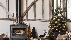 A traditional Christmas living room with wooden beams, wood burning stove and Christmas tree with metallic baubles and star Christmas tree topper