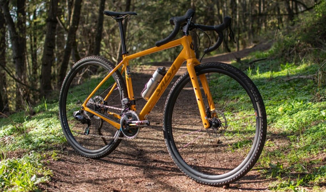yellow salsa warbird gravel bike sat at an angle on a compact woodland track in a quiet wooded area