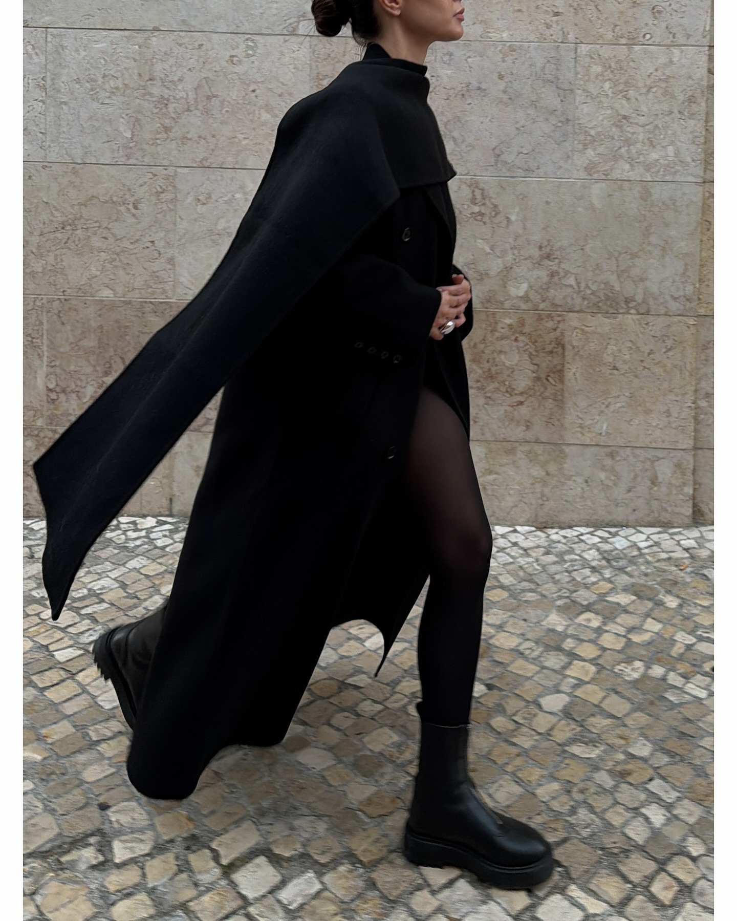 Johanna wears a cape coat, sheer tights, and black combat boot.