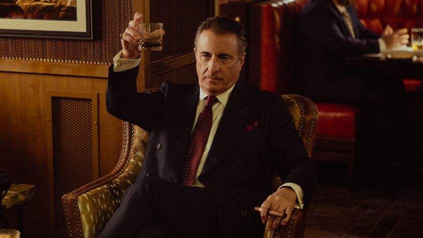 Andy Garcia in Landman holding up a glass with his left hand and holding a cigar in his right hand. 