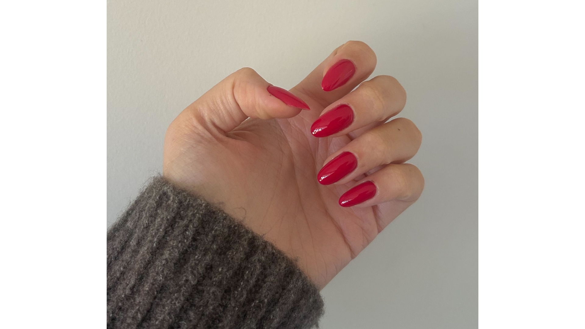 A close-up of Digital Beauty Writer, Sennen Prickett&#039;s hand with long, almond-shaped cranberry nails/ pictured in front of a white background