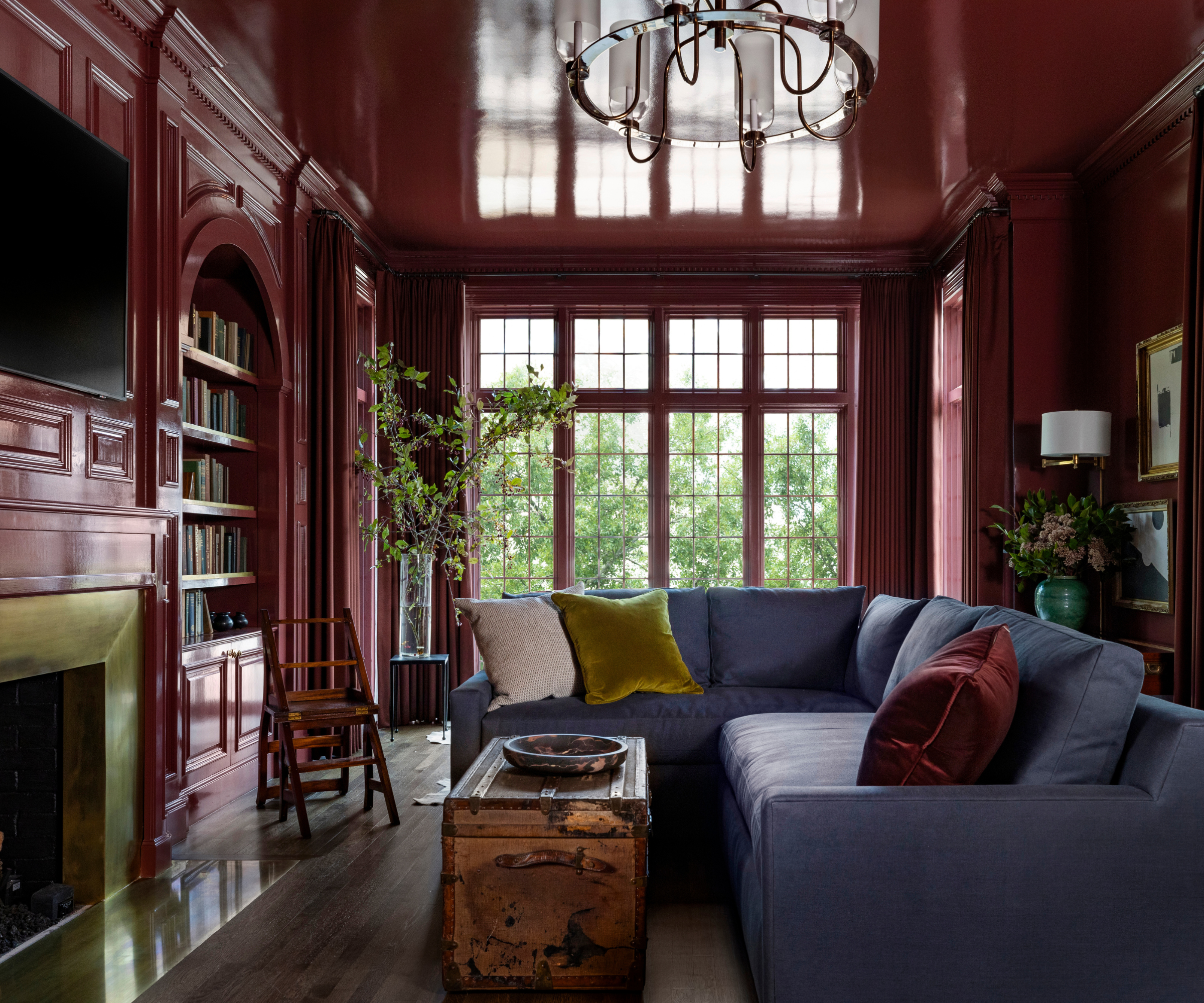 a lounge drenched in deep red high gloss paint, a blue couch with pillows, floor to ceiling windows, and a built-in bookshelf filled with books