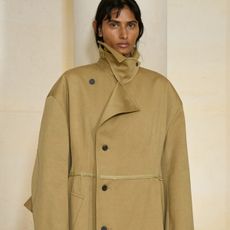 A model at the Carven S/S 26 show wearing a tan trench coat with a funnel neck.