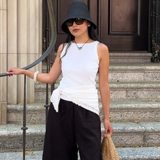 Woman wearing white tank, black shorts, sunglasses in black bucket hat outfit.