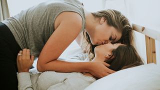 Two women kissing on bed at home after learning how to make missionary sex better
