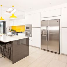 A white kitchen with yellow accents, white cupboards and a stainless steel double door fridge