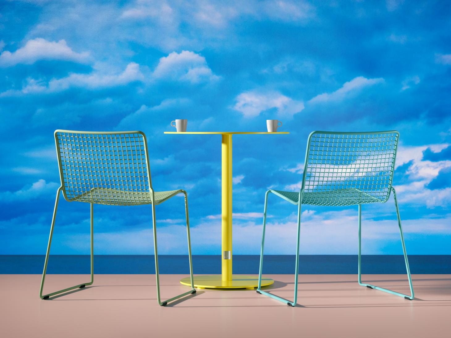 Two metal chairs in green and a small coffee table in yellow, shown in front of a picture of a bright blue sky