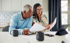 A senior couple reviews finances at the kitchen table.