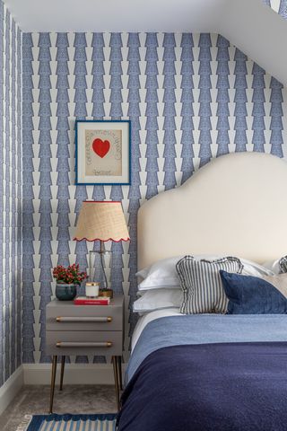 A bedroom with blue patterned wallpaper and white headboard