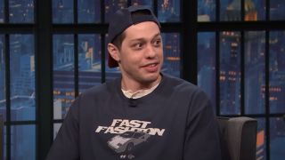 Pete Davidson looking curiously to his right while on Late Night with Seth Meyers. 