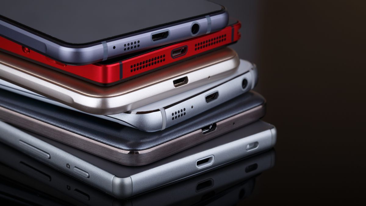 A pile of smartphones from different brands on a black desk