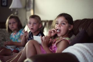 Children eating popcorn as they watch a movie.