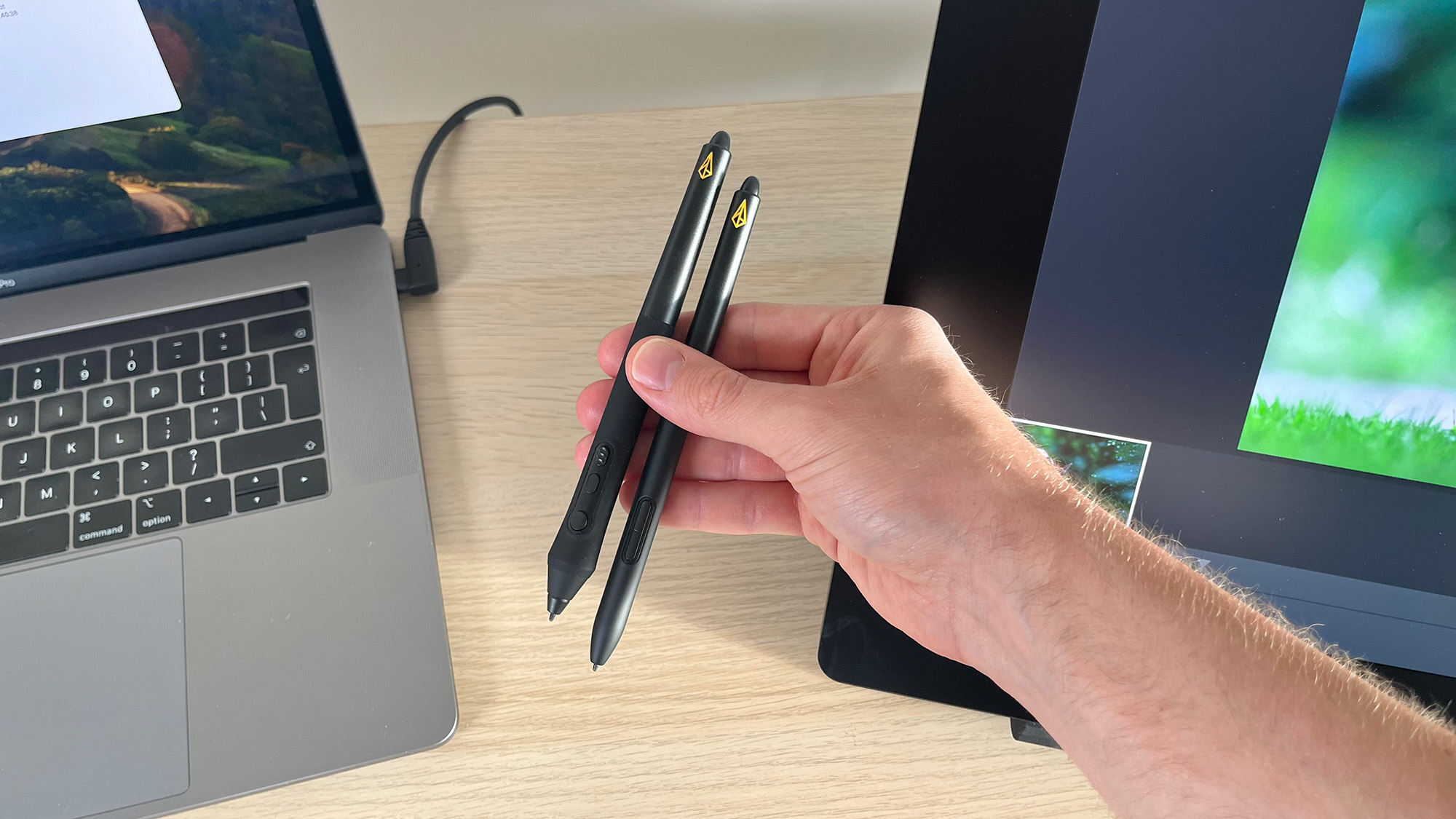 Hand holding Xencelabs styluses next to Pen Display 24+