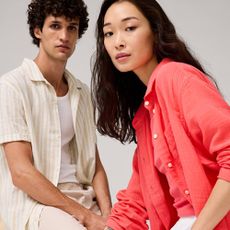 A woman wearing a pink shirt from Gap Factory alongside a man wearing a white vest with a cream and white linen shirt from Gap Factory.