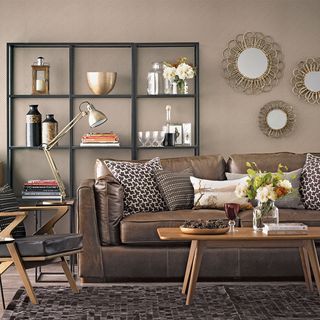 living area with brown sofa and shelf unit and round mirror and coffee table