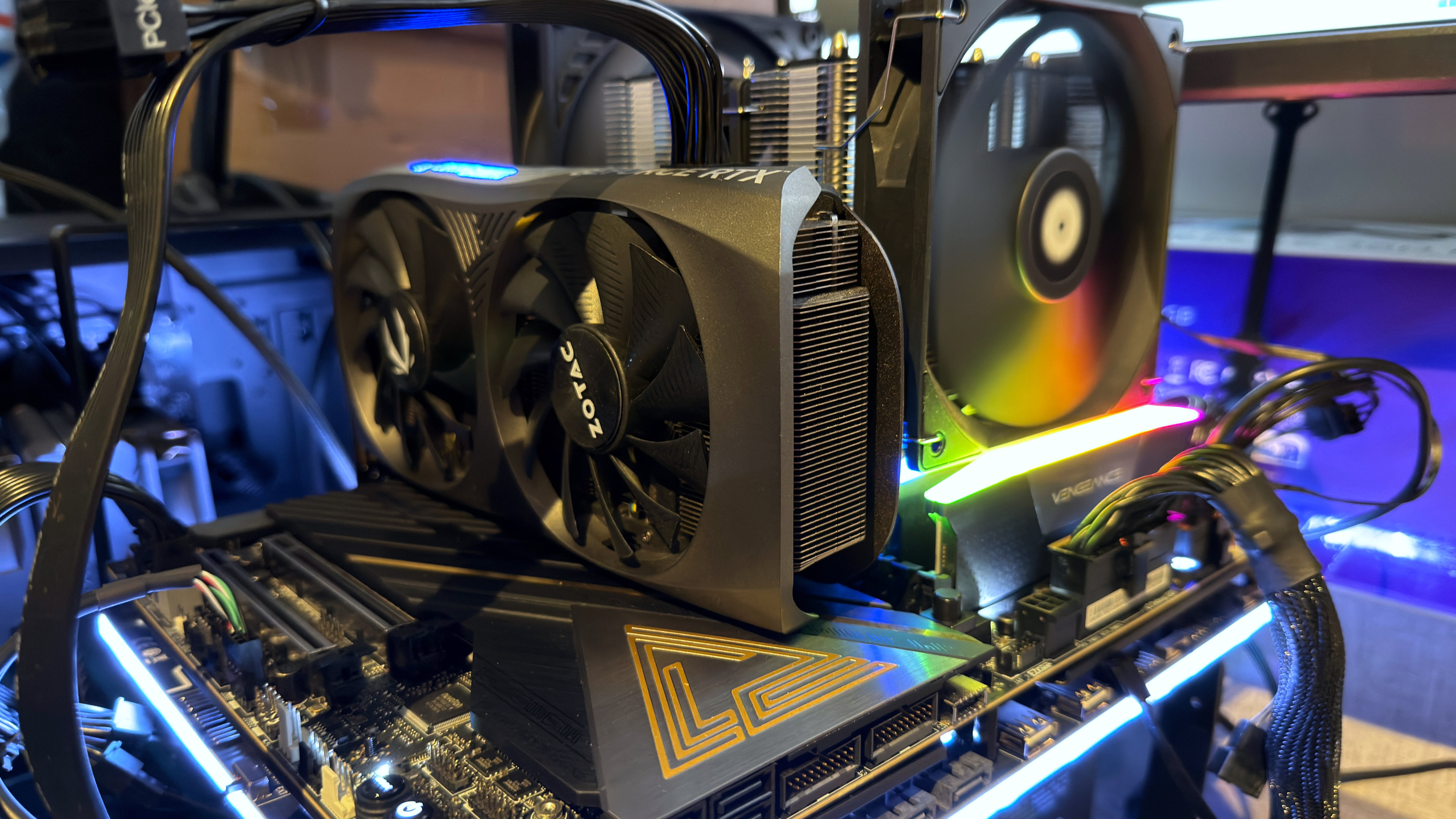 A photo of an open-chassis test bench PC, showing a motherboard, graphics card, DRAM DIMMs, and a fan in a CPU cooler