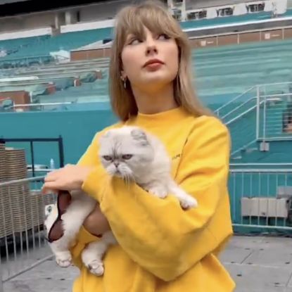 Taylor Swift wears a yellow sweatshirt and a pair of wide leg jeans 