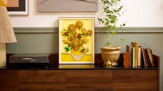 Lego Sunflowers on a wooden surface beside a plant, books, lamp, and record player