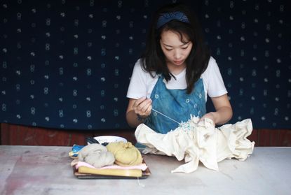 A portrait of Chinese artist Fanglu Lin working on a textile piece featuring tying techniques from the women from the Bai minority of China