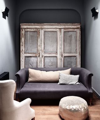 An example of dark living room ideas showing small grey furniture in front of a distressed wood cabinet