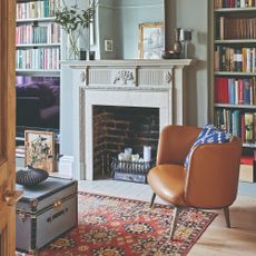 A living room with a light-painted fireplace surrounded by a built-in library and a brown leather armchair next to it