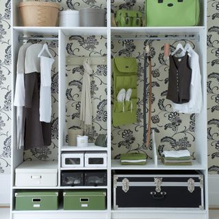 An open wardrobe with storage boxes and the back wall covered in a floral wallpaper