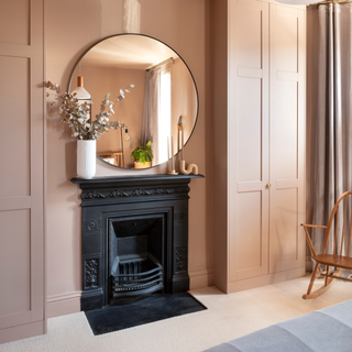 Black fireplace with circular mirror above. The walls are drenched in dusky pink