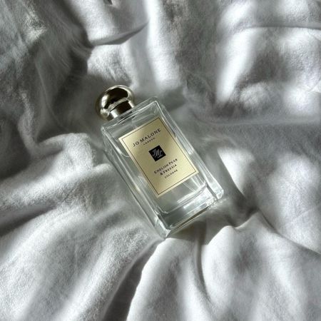 a Jo Malone London perfume bottle sitting on a white linen sheet in natural sunlight