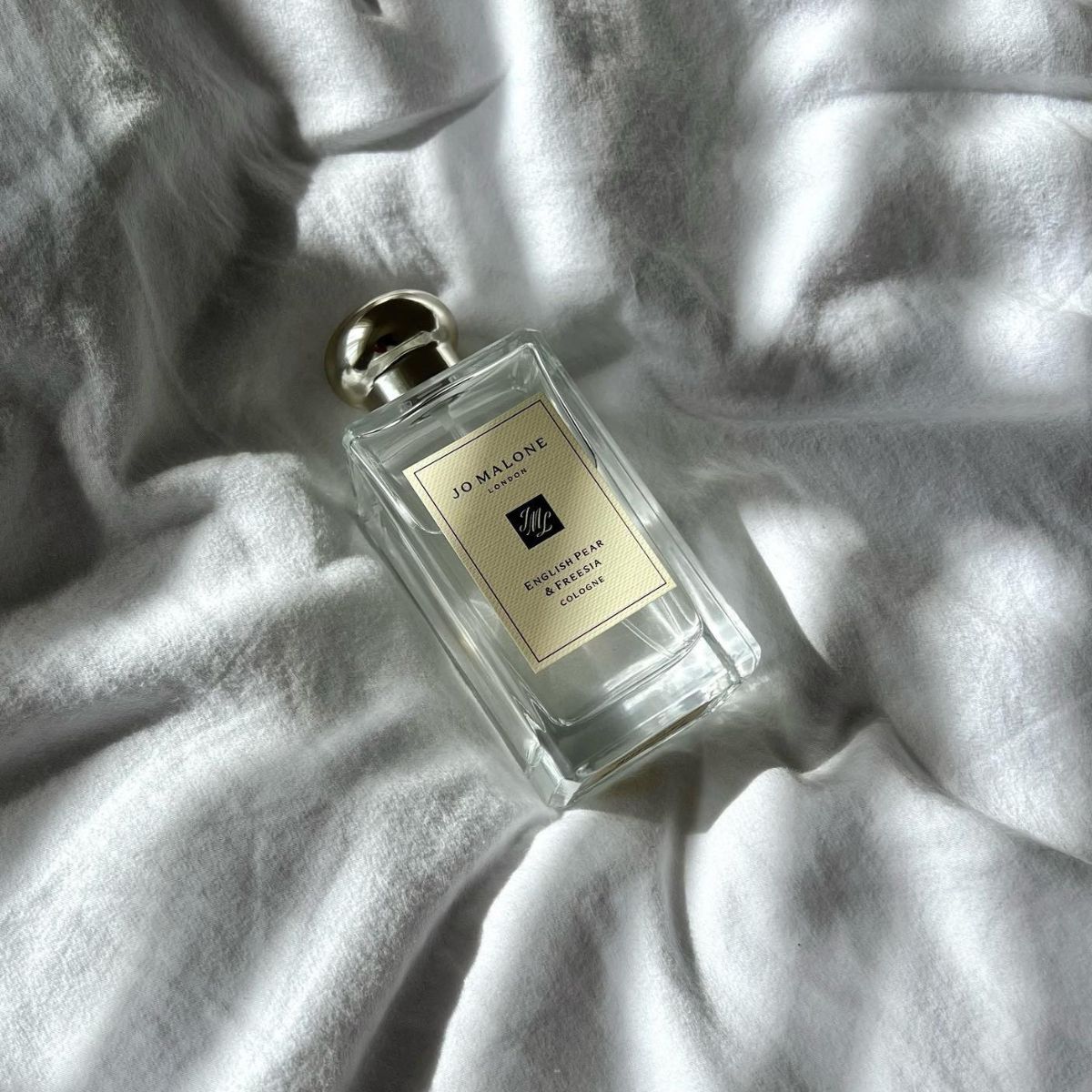 a Jo Malone London perfume bottle sitting on a white linen sheet in natural sunlight