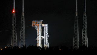 a large white rocket sits vertical on a launch pad at night