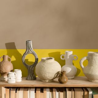 A ceramic vase display on a wooden bookcase with a two-toned wall behind in beige and yellow