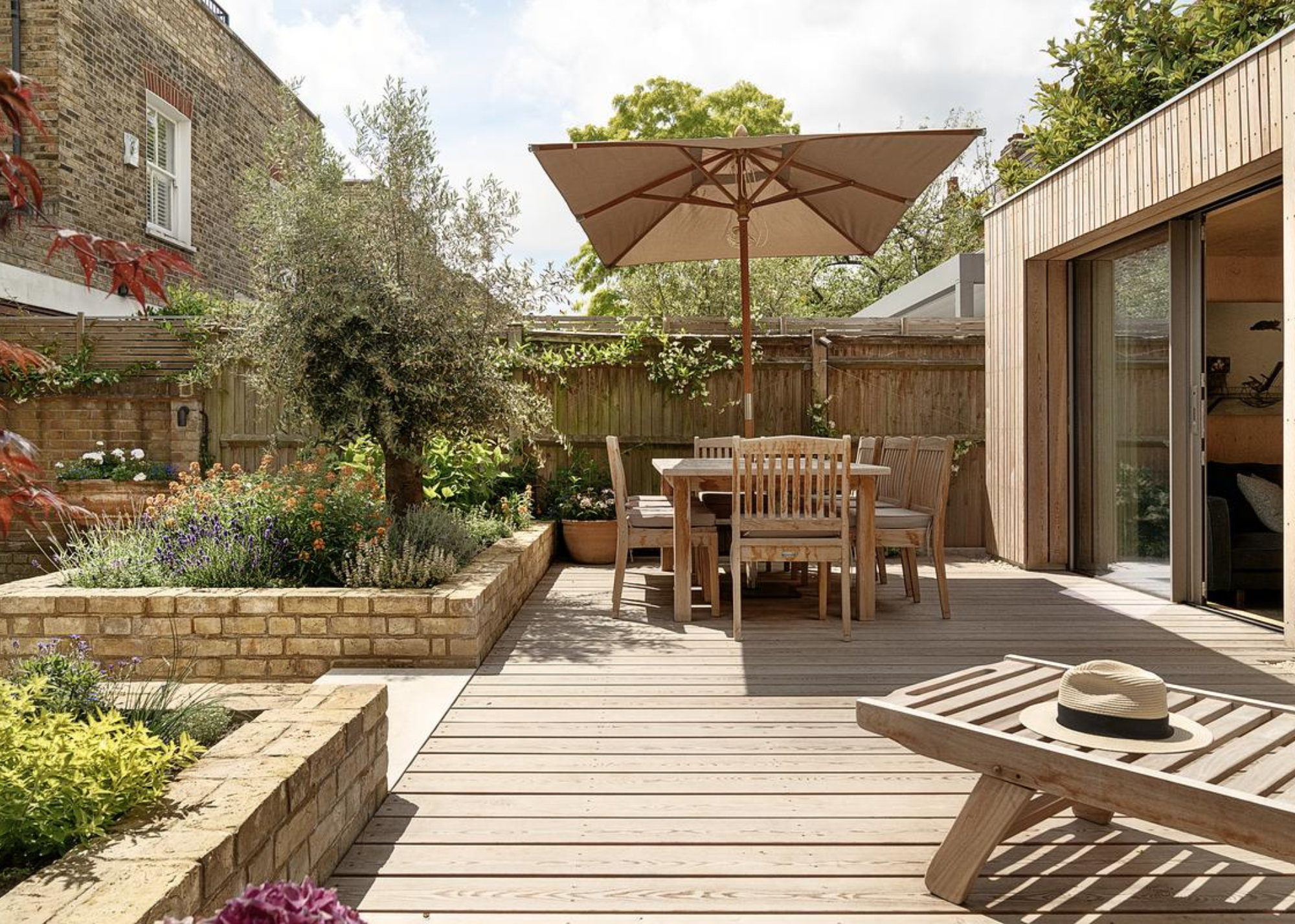 urban garden with wooden decking, wild flowers, wooden outdoor furniture and a wooden garden room in the back