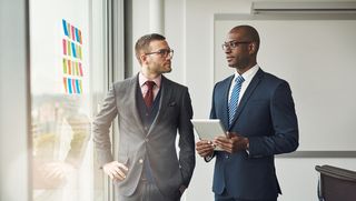 Two businessmen in an office planning by a window with sticky notes on it