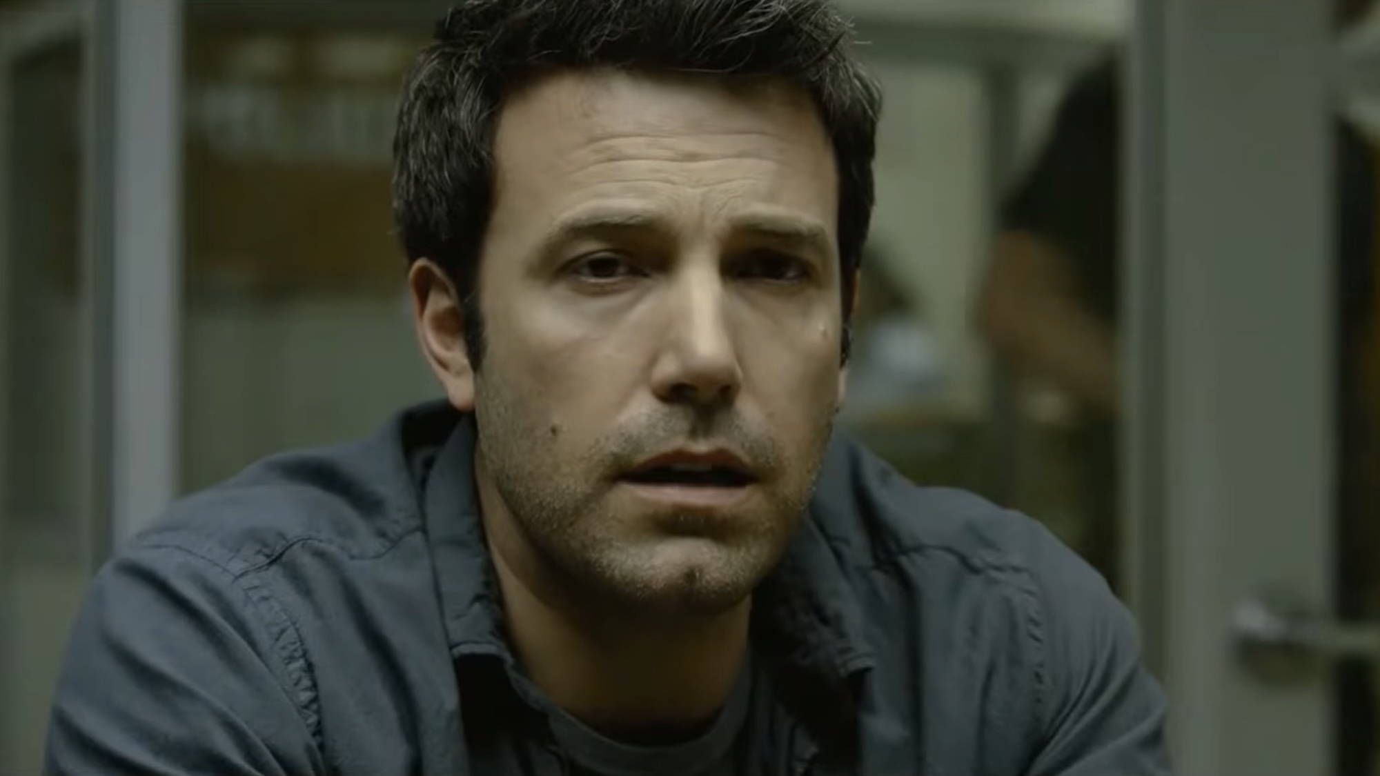 Ben Affleck in a grey shirt talking to a cop in Gone Girl. 