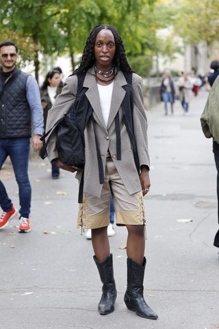 woman wearing blazer, t-shirt, bermuda shorts, and black cowboy boots