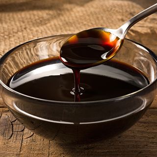 Molasses dripping off metal spoon into glass bowl
