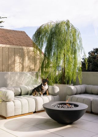 A balcony with plush outdoor sofas, a firepit and a dog