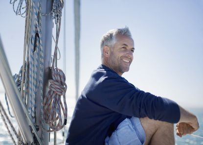 A middle-aged man smiles while sitting on the deck of a sailboat.