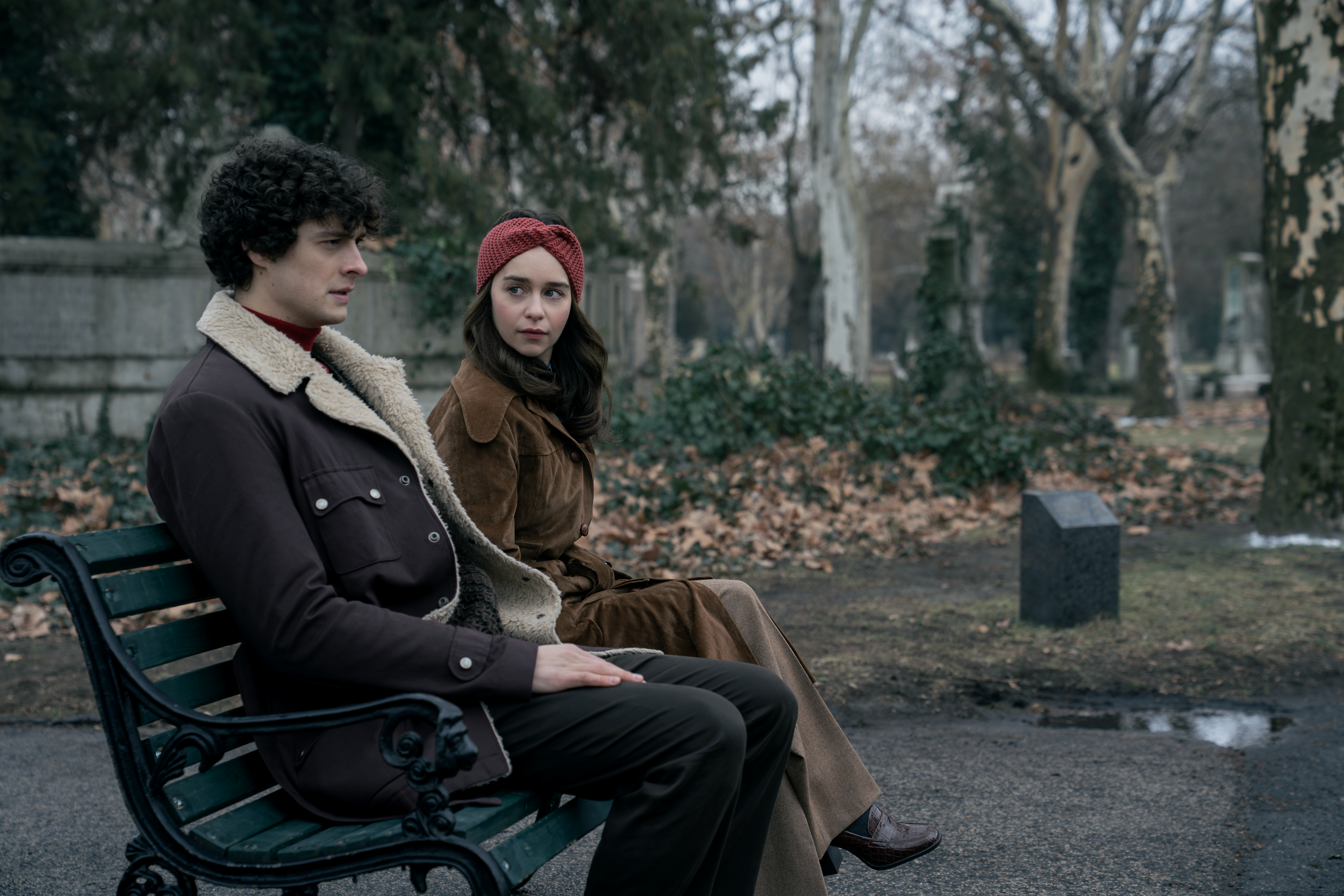 A series of film stills and photographs from a 1970s-inspired set featuring vibrantly decorated interiors with layered furniture and warm lighting, along with characters dressed in vintage clothing whether indoors or at parks, in cards, or at markets outdoors.