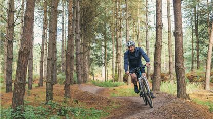 An older man rides a bicycle on a wooded trail.