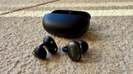 The Earfun Clip 2 earbuds next to their charging case on a stone surface