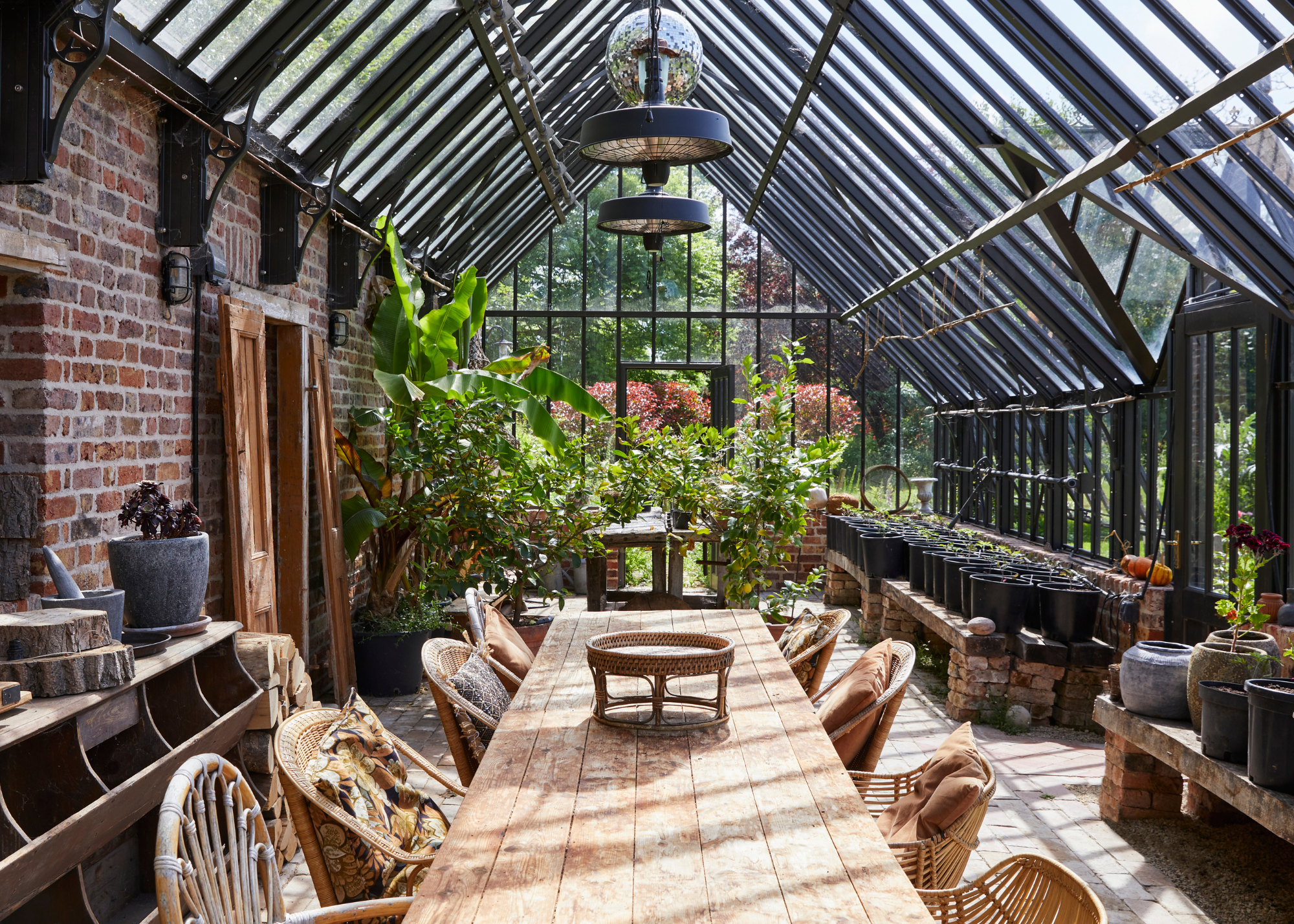 modern greenhouse with a black frame and a brick foundation, with a disco ball and a long dining table in the middle