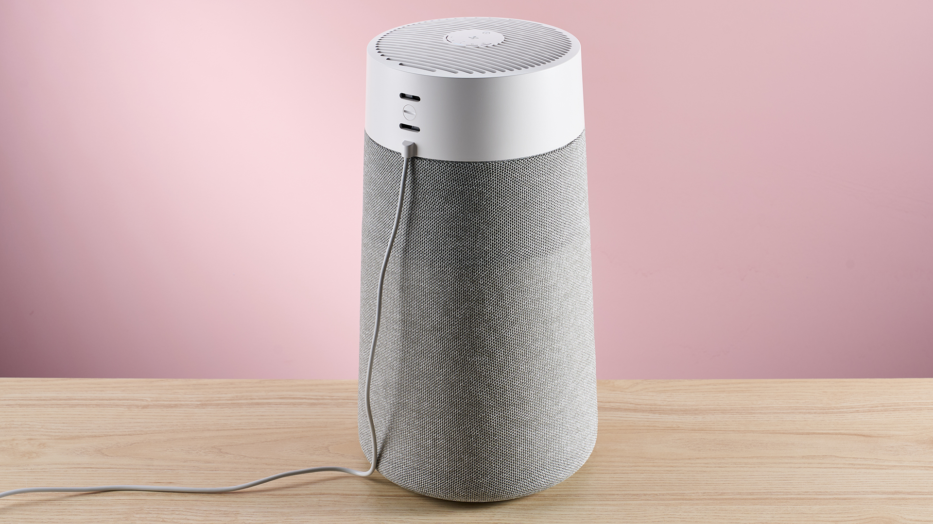 The large Blueair air purifier sits with its back turned toward the camera on a wood surface against a pink background.