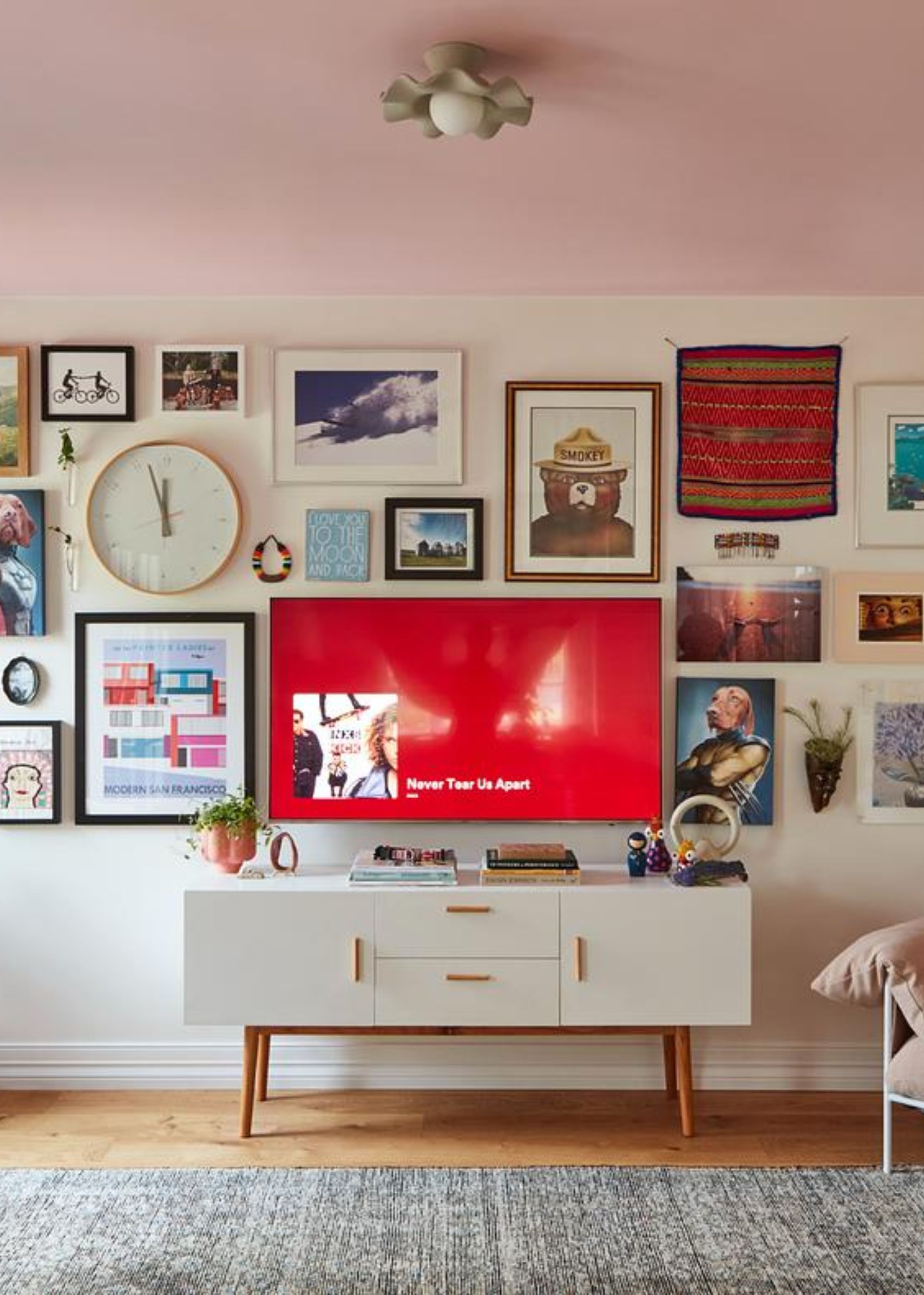 A gallery wall with a tv in the middle as well as a console in the middle with cabinets and drawers
