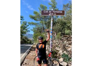 Dr Auriel Forrester pointing to a Coll de Fermenia 515m sign with her bike behind her