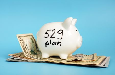 A piggy bank with the words "529 plan" written on it, sitting on top of a small pile of cash.