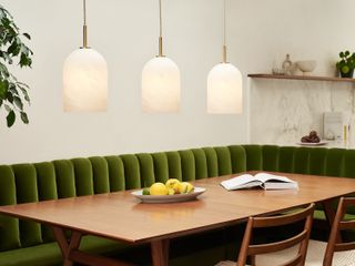 A wooden dining table with three pendant lights and green sofa