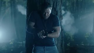 Alan Ritchson as Jack Reacher evading gunfire behind a tree on Reacher