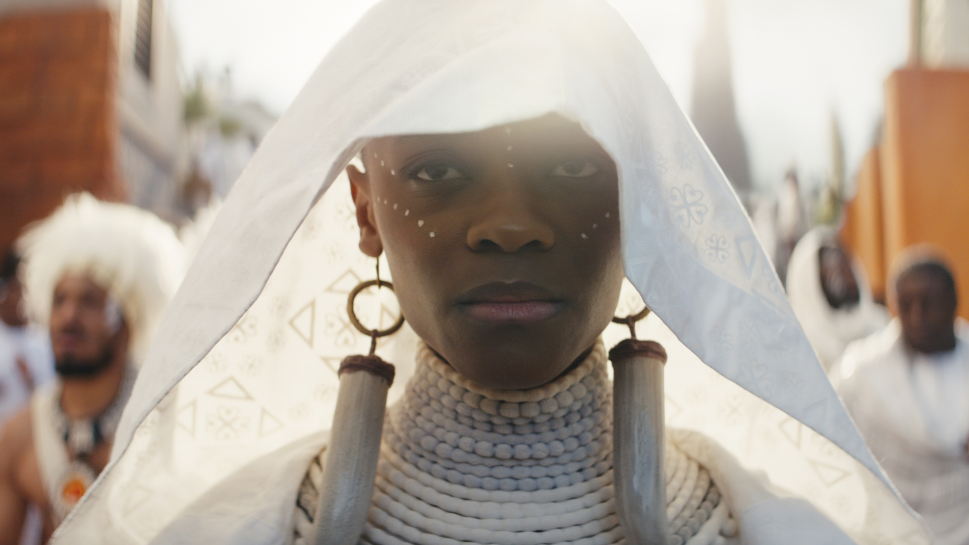 Shuri usa una capucha y una capa blanca mientras camina por un sendero durante la procesión fúnebre de T'Challa en Black Panther 2